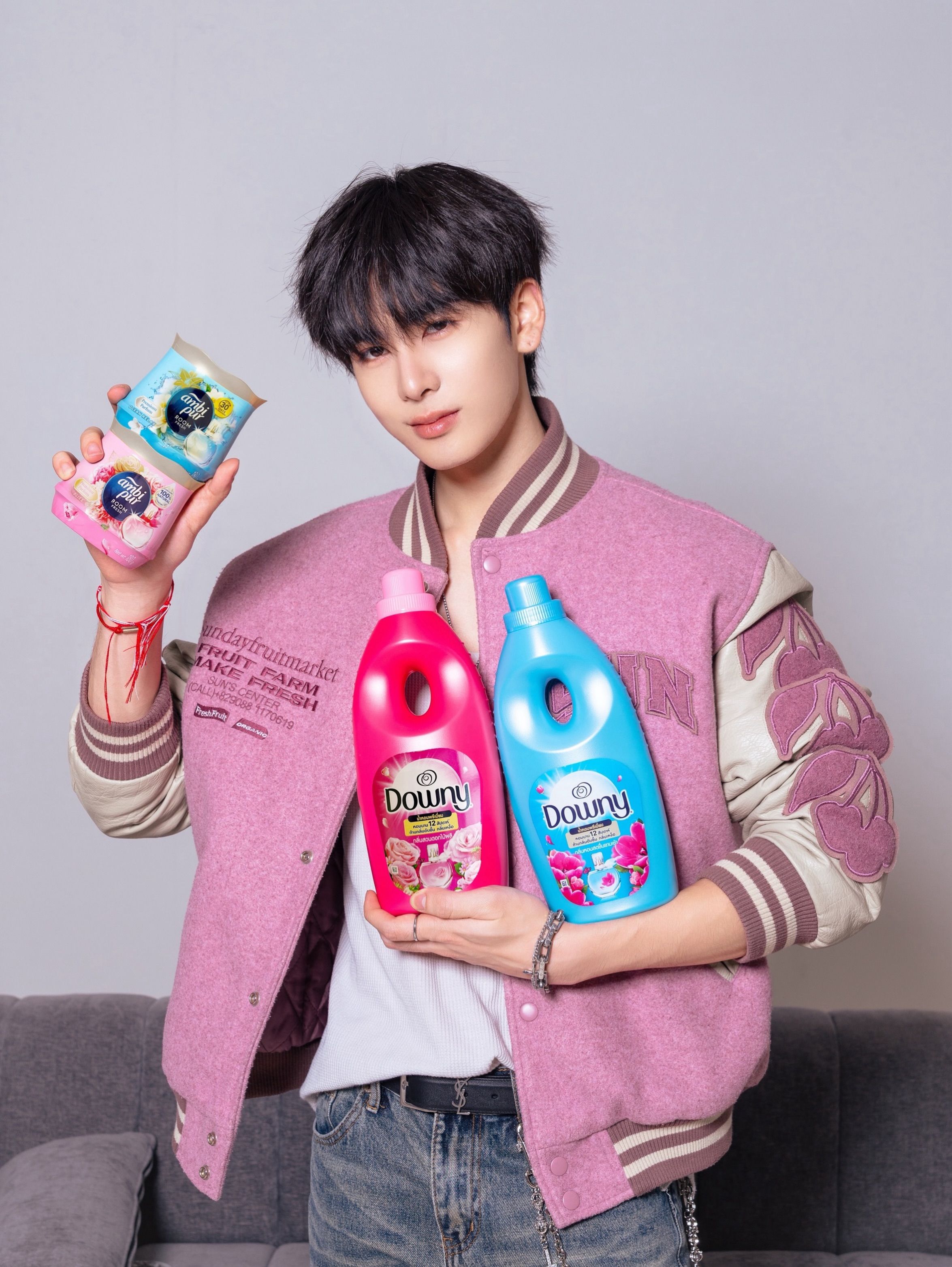 Jeune homme aux cheveux courts noirs portant une veste de baseball rose et un jean tenant des après-shampooings et des parfums