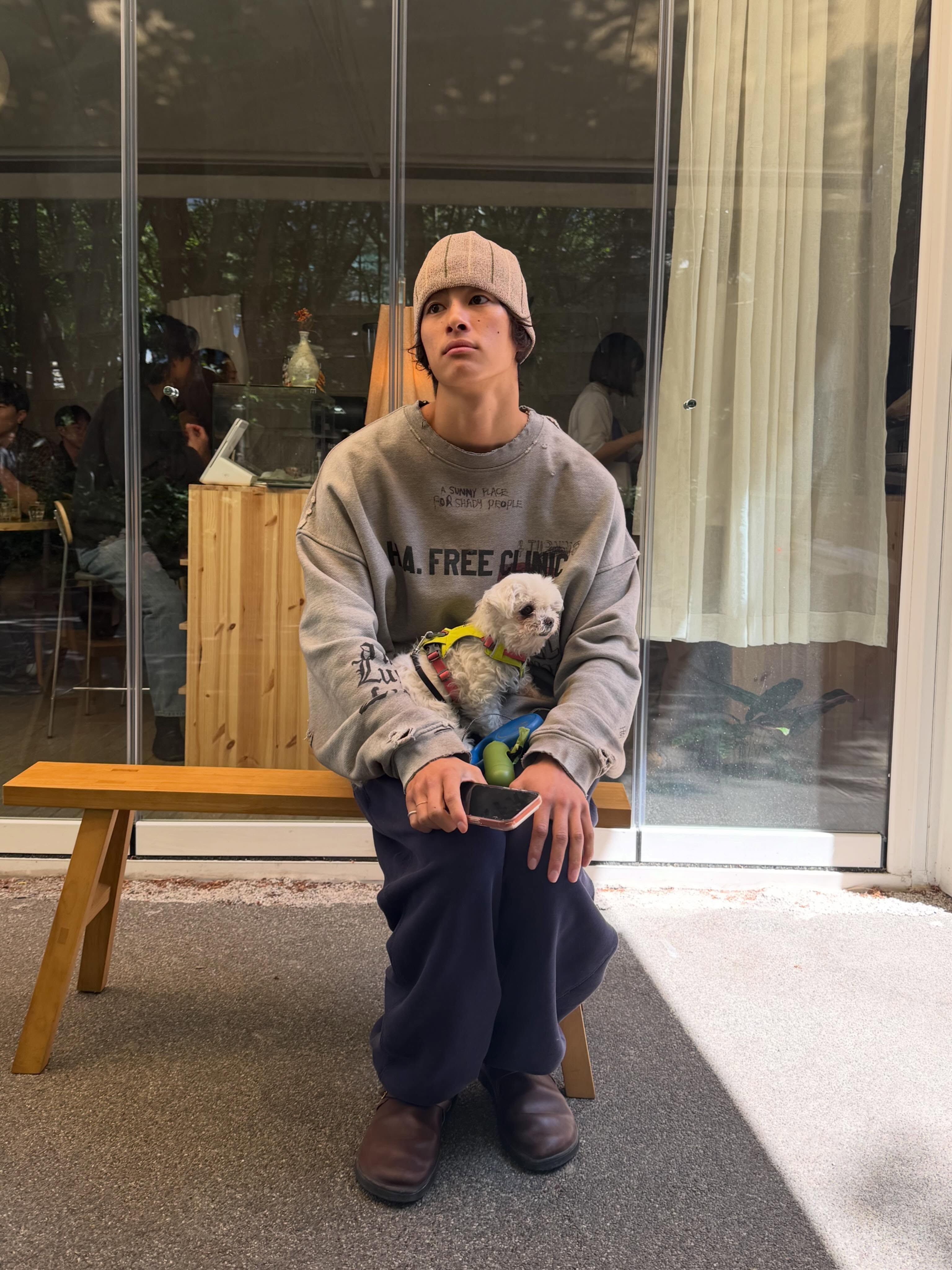 若い男性がニット帽をかぶりグレーのスウェットを着て白い子犬を抱えて屋外に座っている
