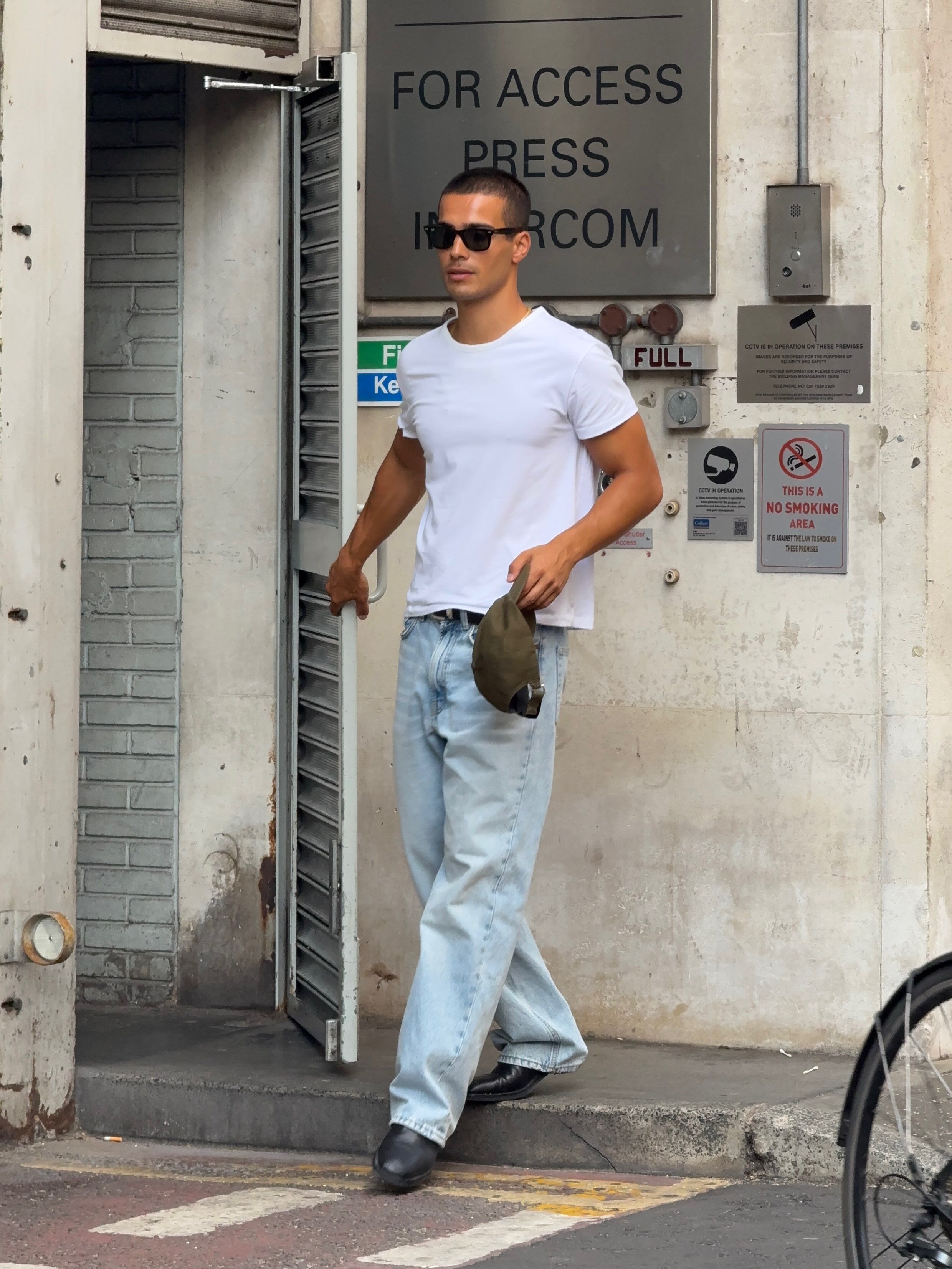 Jeune homme musclé en t shirt blanc et jean bleu clair debout à l'entrée du bâtiment