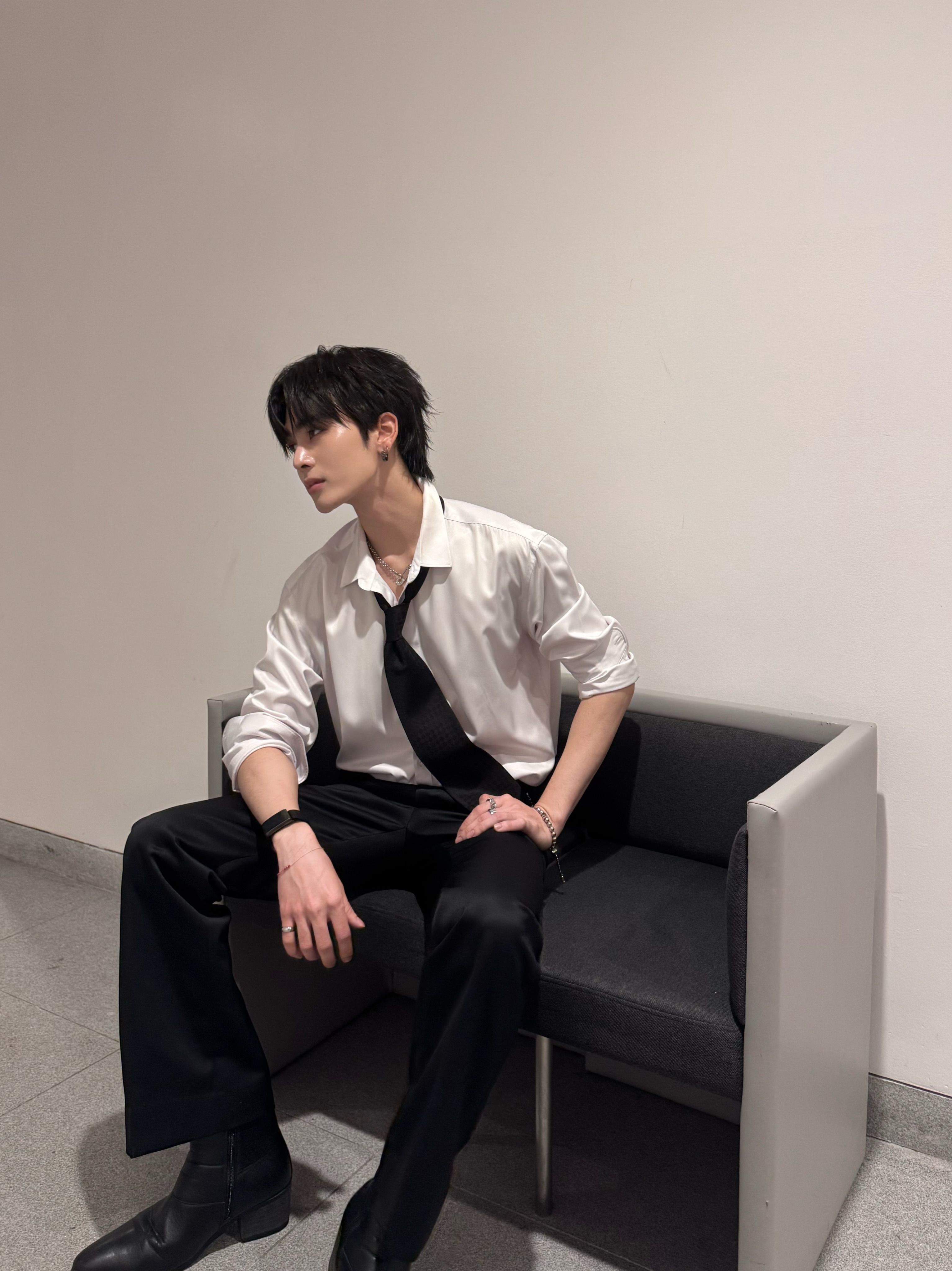 若い男性が白いシャツ黒いネクタイ黒パンツ短靴を着てソファに横座り