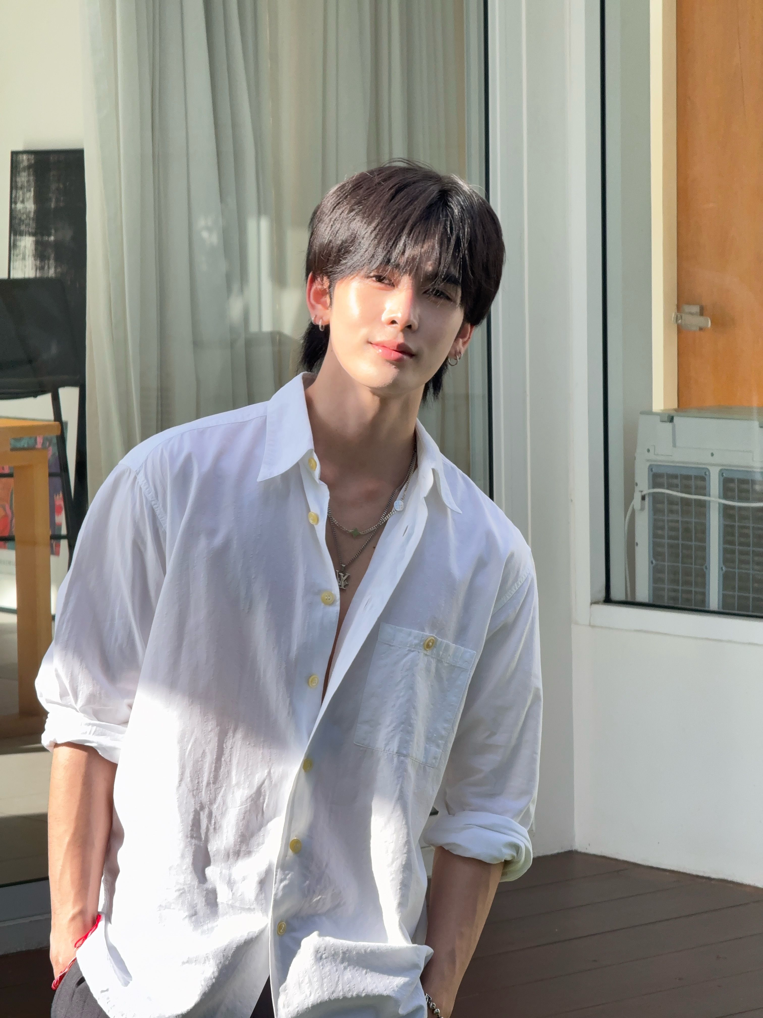 年轻男子穿白色衬衫搭配多层项链和红绳手链站在户外阳台