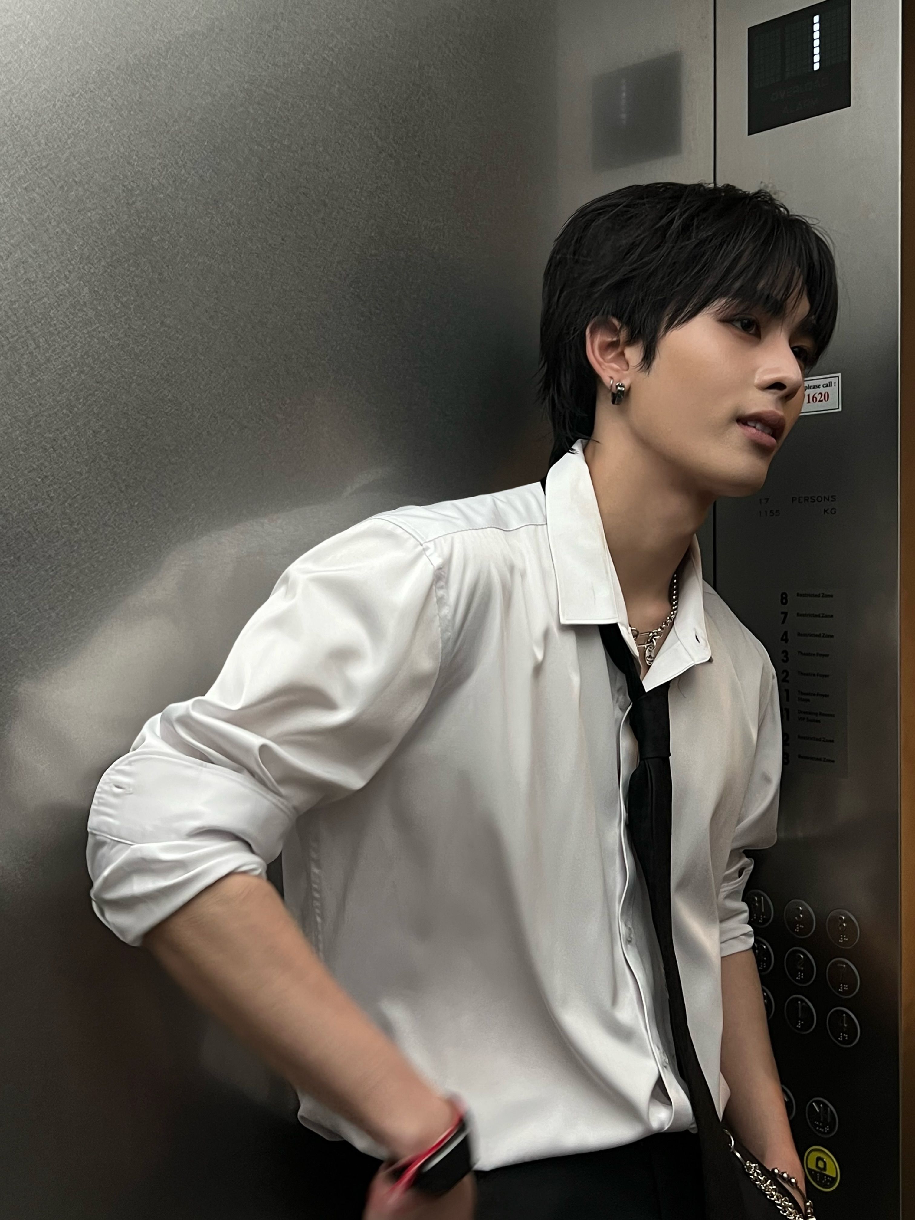 若い男性が白いサテンシャツと黒いネクタイで壁にもたれている